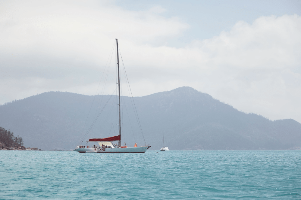 Sailboat with red sail on turquoise water, mountains in background.