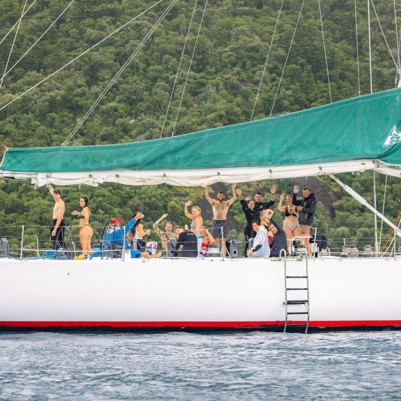 People on a sailboat with a green canopy, set against a background of lush green hills.